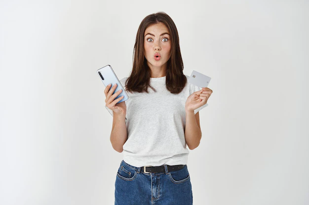 compras-linea-mujer-joven-morena-haciendo-compras-internet-tarjeta-credito-smartphone-mirando-al-frente-divertido-pared-blanca_176420-42721