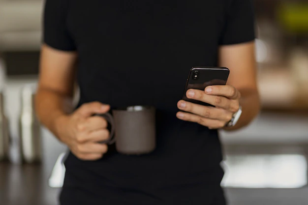hombre-enviando-mensajes-texto-su-telefono-mientras-sostiene-taza-cafe-negro-otra-mano_53876-146602